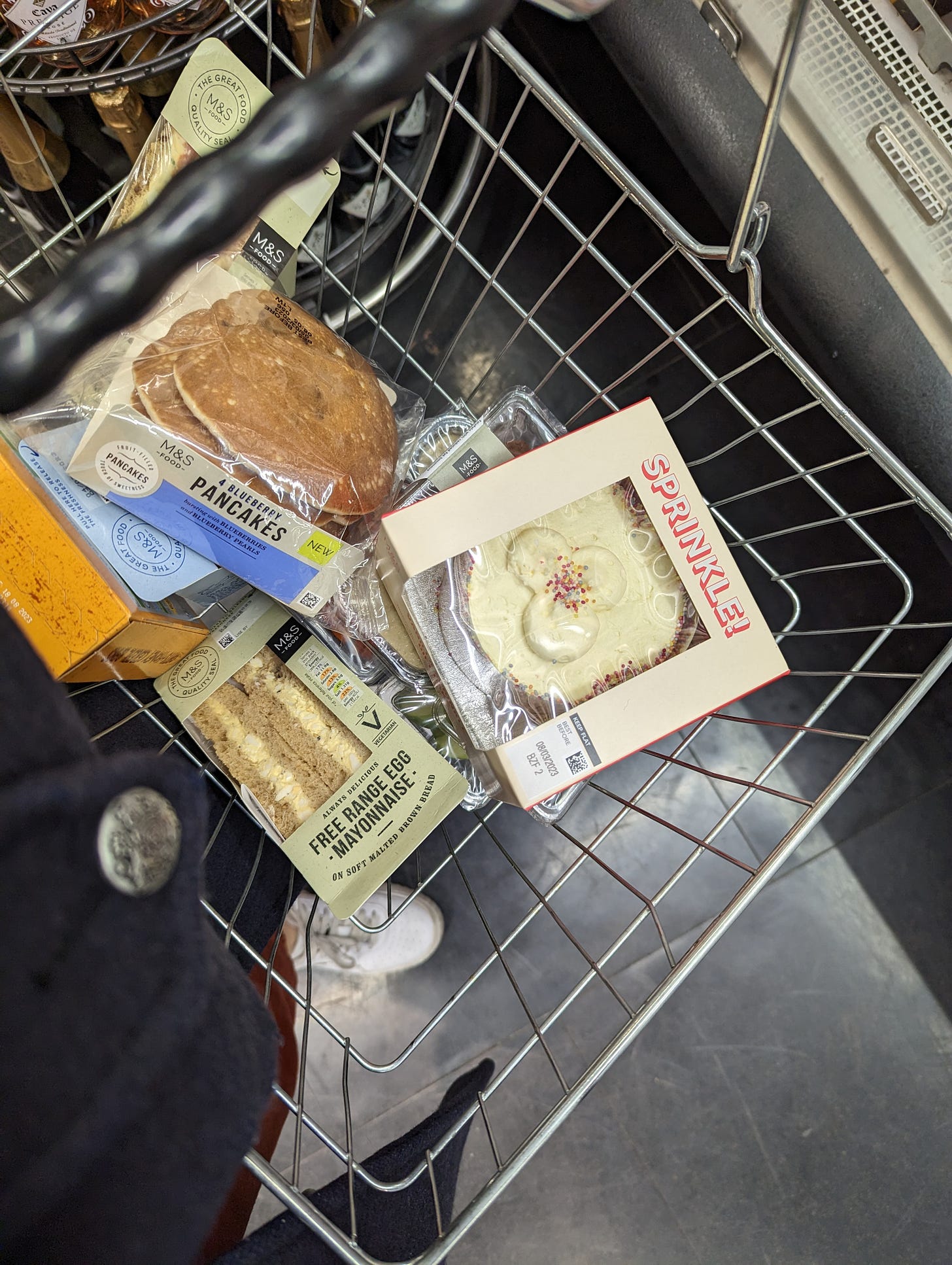 A picture of a grocery basket filled with pancakes, cakes, sandwiches and other pre-packaged products from M&S.