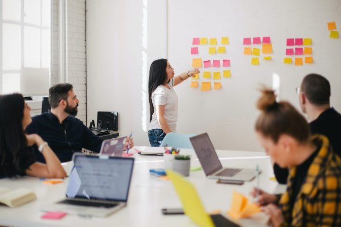 Person next to sticky notes with other people seated around a table looking in that direction