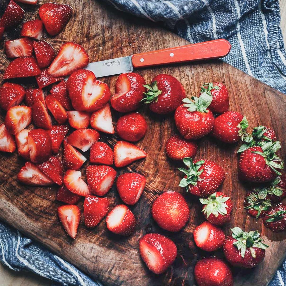 A cutting board covered in whole and sliced strawberries