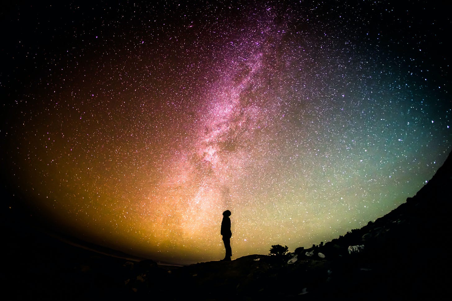 A person standing on a slope looking at the Milky Way and stars in the night sky.