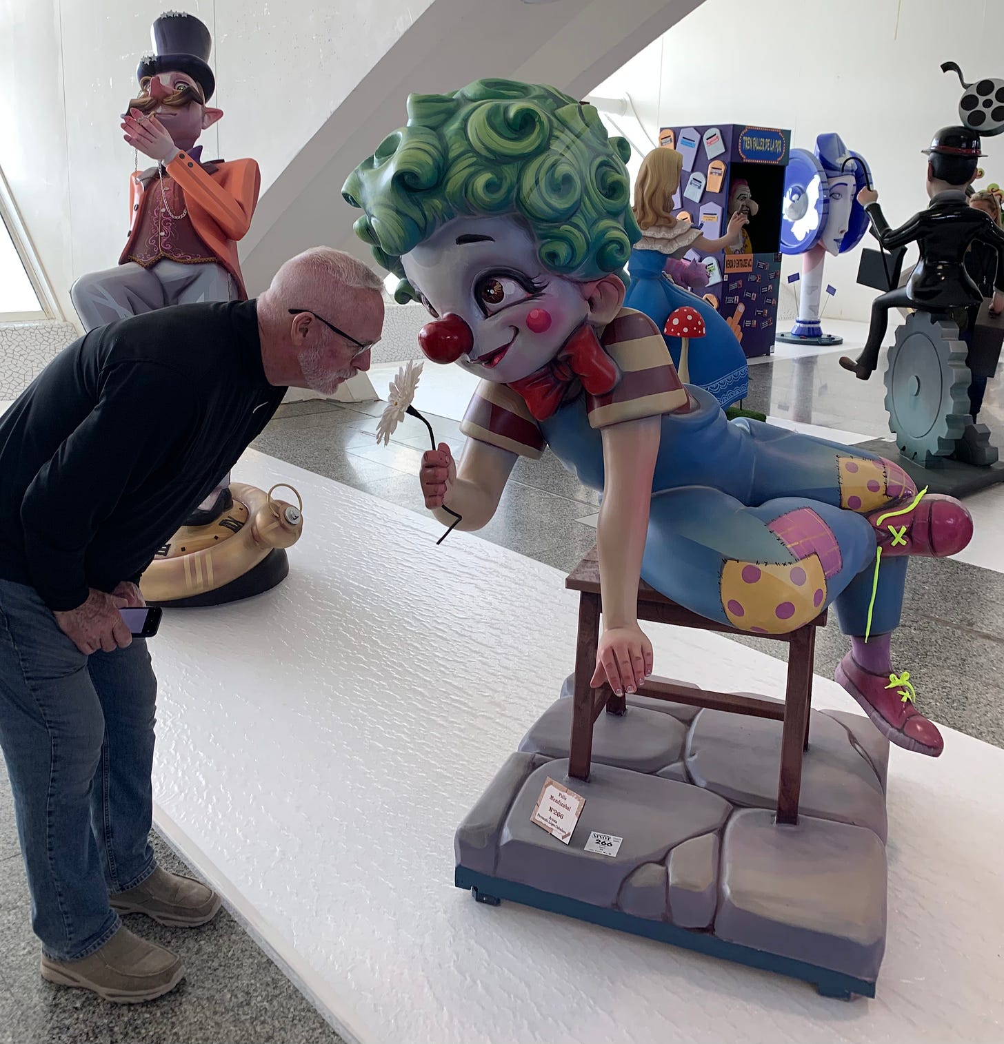 Jim leans over to smell a flower proffered by a childlike green-haired clown