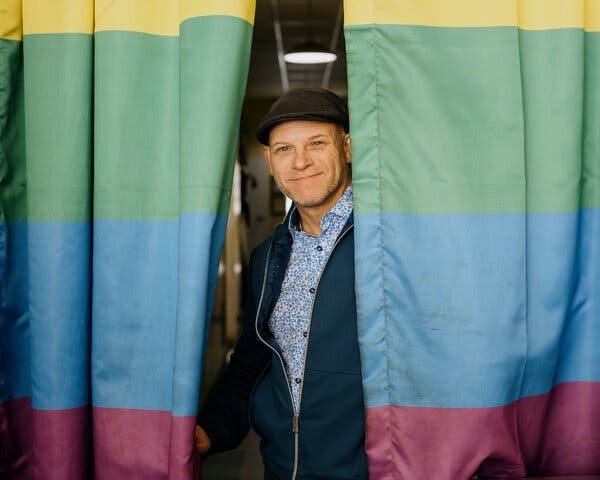 Ryan Jones between large drapes in rainbow colors.