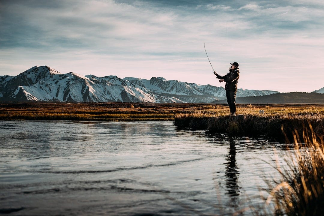 landscape photo of man fishing on river near mountain alps