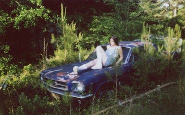 Ethel Cain sitting on a blue car in a field