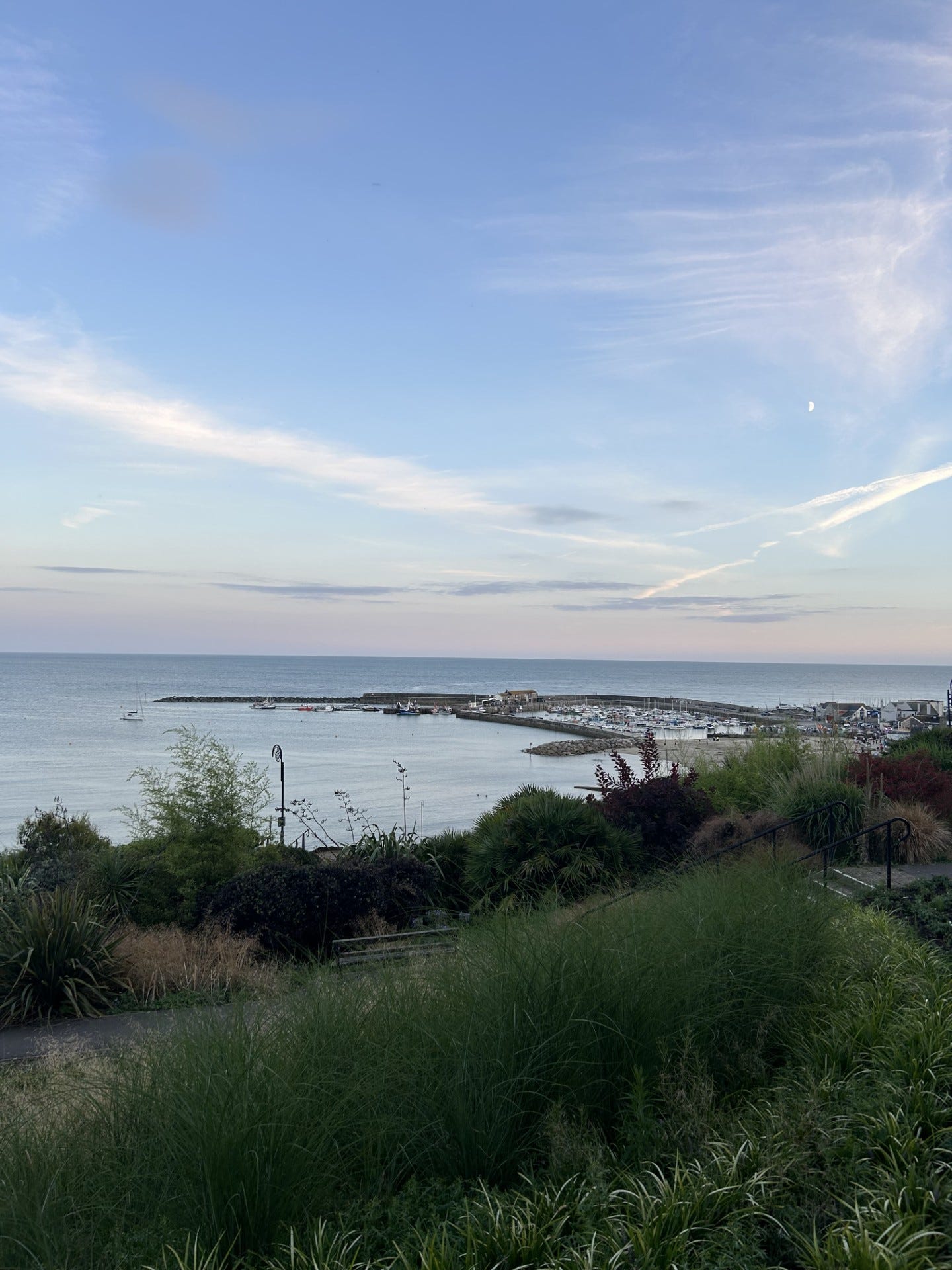 A serene evening view of Lyme Regis Harbour, with calm waters reflecting the warm hues of dusk