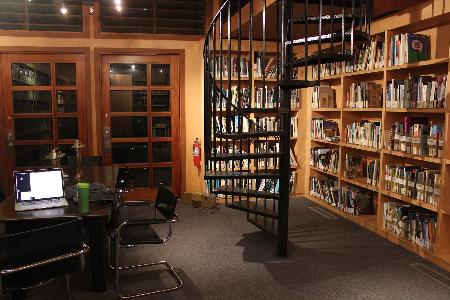 a color photo of a library with a desk and spiral staircase