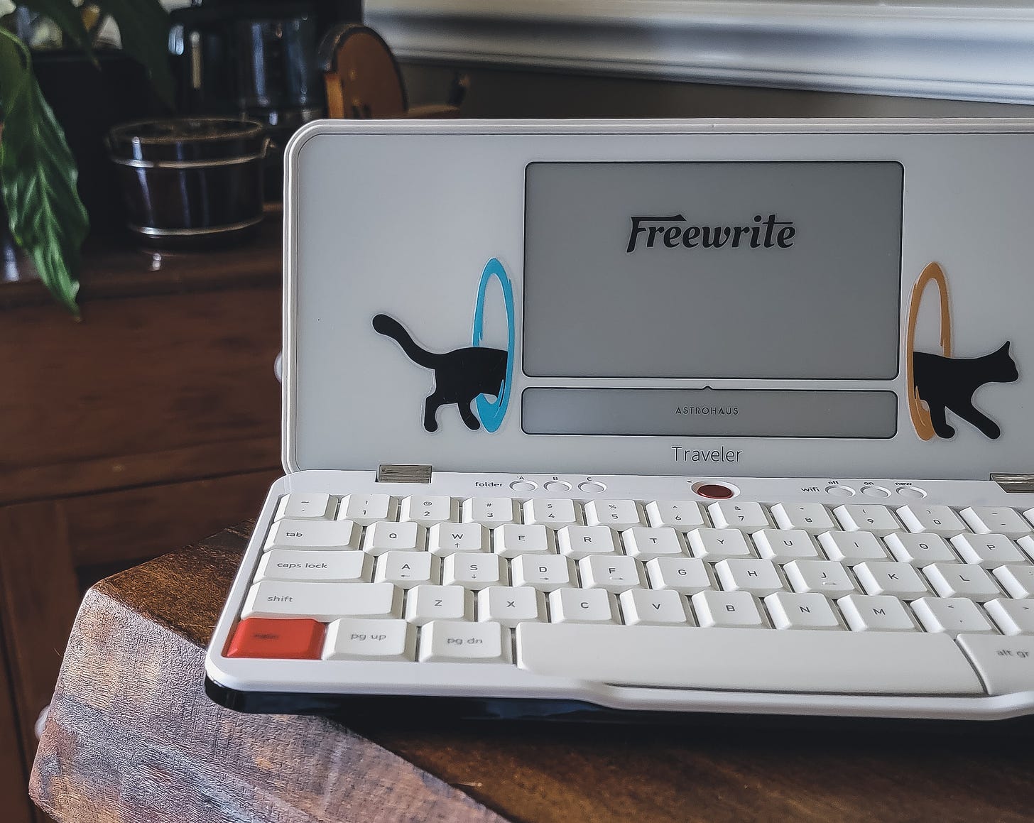 My Freewrite Traveler device sitting on a table. There are portal cat stickers on either side of the screen.