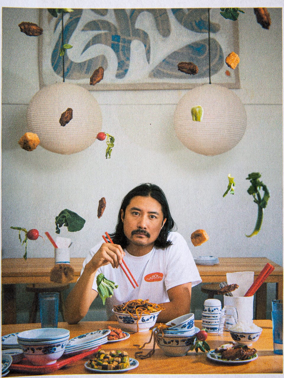 Man eating noodles surrounded by ingredients floating in suspension.