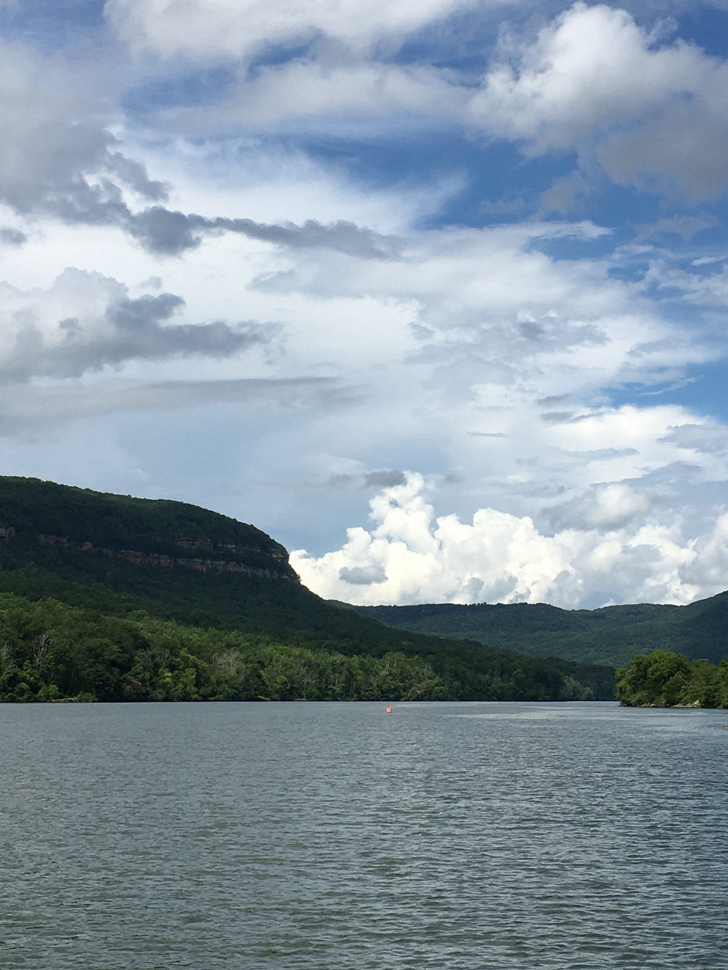 image of a river, with mountains surrounding, and a blue sky full of puffy clouds some bright white, some more gray