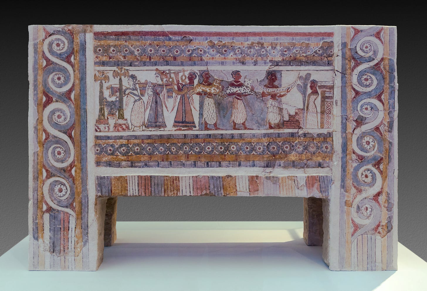 Side view of the Hagia Triada sarcophagus, a rectangular footed limestone container with a fresco painted on the side. The painted decoration includes spirals, rosettes, and a funeral scene with a priestess pouring a libation, a musician playing a lyre, and men bringing offerings.