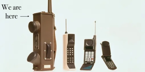 Přehled mobilních telefonů od těch úplně nejstarších. K nejstaršímu z nich, který vypadá jako bezdrátový polní telefon směřuje šipka s nápisem: Jsme tady.