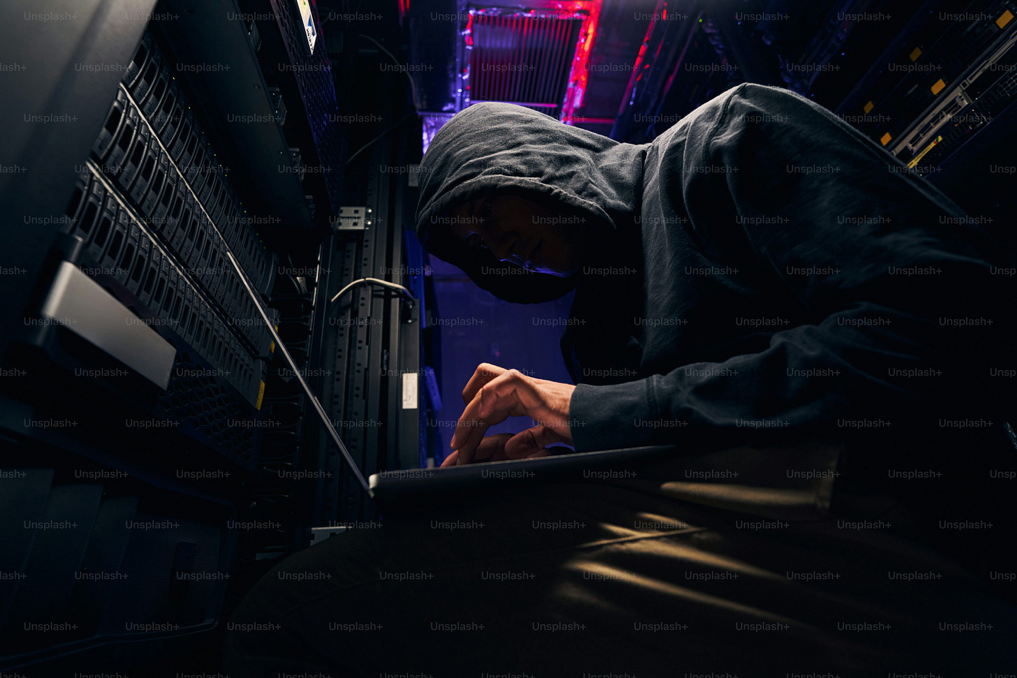 Low angle of hacker installing malicious software on data center servers using laptop Low angle of hacker installing malicious software on data center servers using laptop