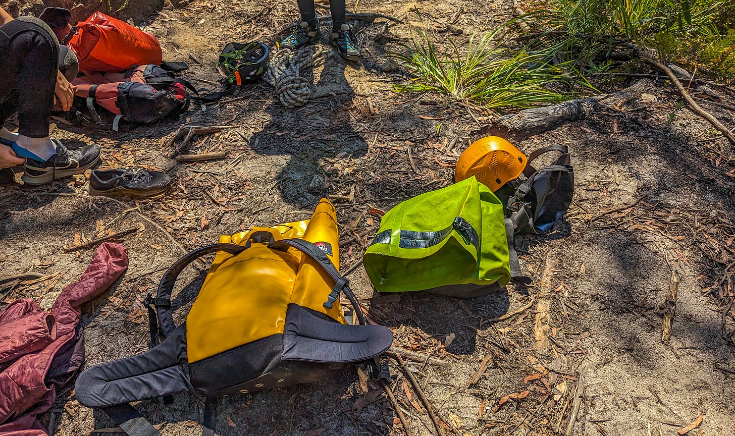 Backpack, dry bag, helmet, thermal socks, and other equipment on the ground. 