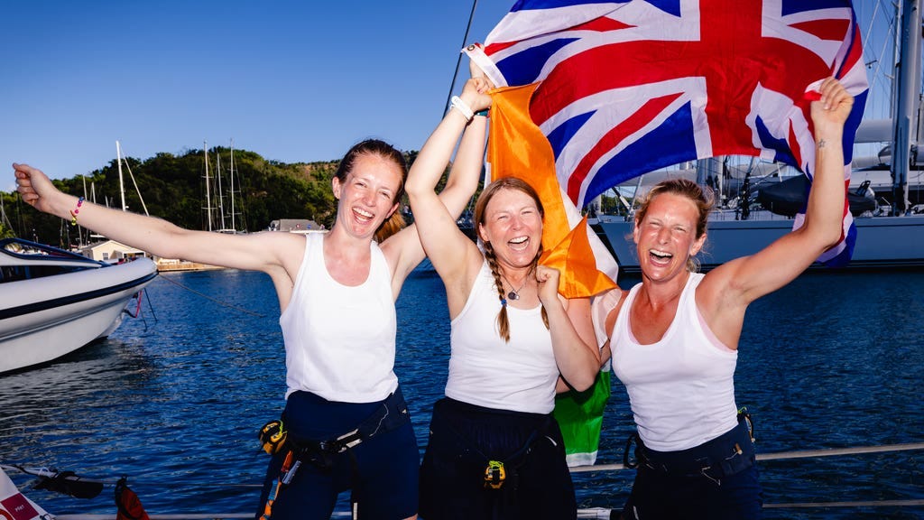 Female rowing trio waving the Union Jack flag whilst stood on a row boat