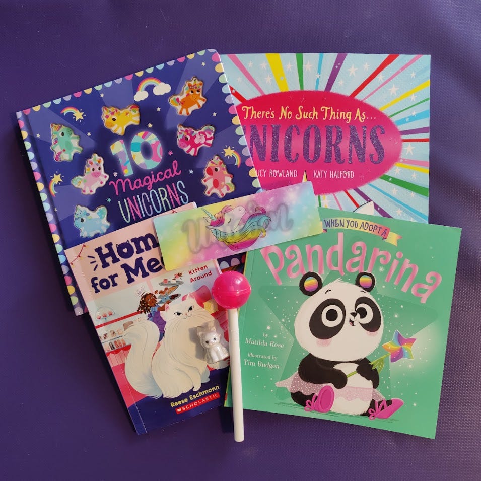 A pile of books arranged two over two with a holographic bookmark featuring a unicorn and the word unicorn and a white pen with a bulbous pink cap that looks like a large dumdum lollipop. The books are, starting in the upper left corner and working clockwise, 10 magical unicorns, There's No Such Thing As Unicorns, When You Adopt A Pandarina, and Home for Meow.