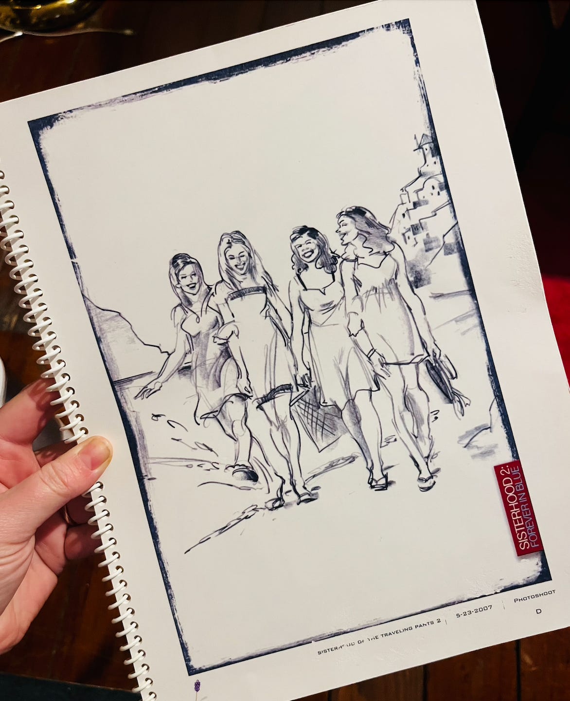 A spiral-bound book. The cover shows a sketch of four women in sundresses walking on a beach together, smiling. In the corner of the cover is the text, "Sisterhood 2: Forever In Blue."