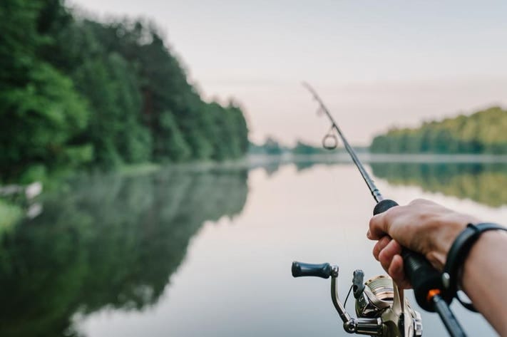 Fisherman with rod, spinning reel on the river bank. Sunrise. Fishing for pike, perch, carp. Fog against the backdrop of lake. background Misty morning. wild nature. The concept of a rural getaway.