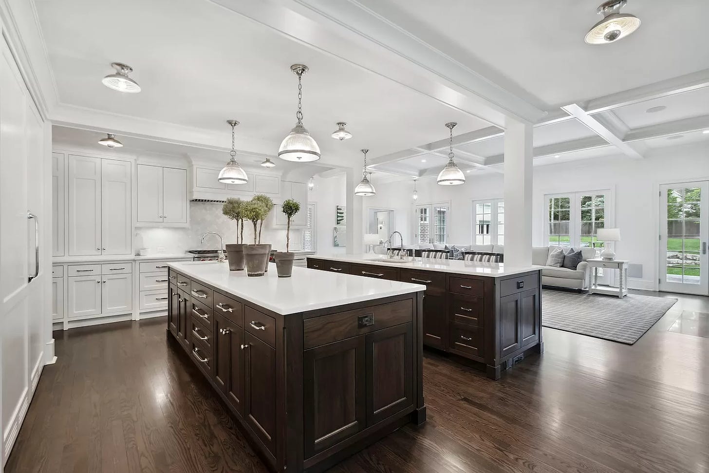 A very, very white open space. The kitchen has white cabinets and then two islands that have dark brown wood and white countertops. It is sterile.