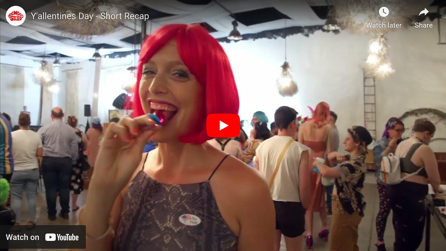 Screenshot of the YouTube video from Y'allentines Day featuring a young intersex woman Alicia Roth-Weigel wearing a shocking pink bob wig and eating a matching pink RingPop with a dancing crowd in the background.