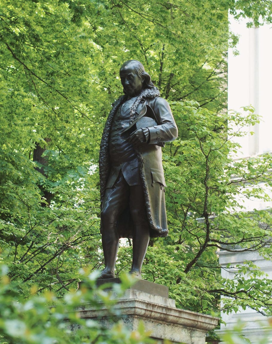 man in coat statue near green trees during daytime