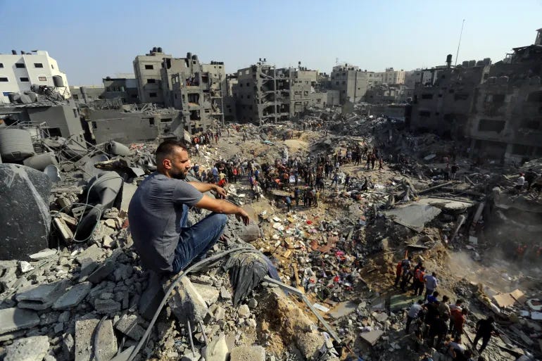 A man sits on the rubble as others wander among debris of buildings that were targeted by Israeli airstrikes in Jabaliya refugee camp, northern Gaza Strip, Wednesday, Nov. 1, 2023 [AP Photo/Abed Khaled]