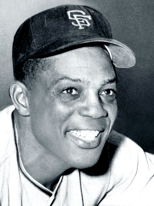 Black-and-white portrait photo of a broadly-smiling man wearing a dark-colored baseball cap with SF embroidered on it