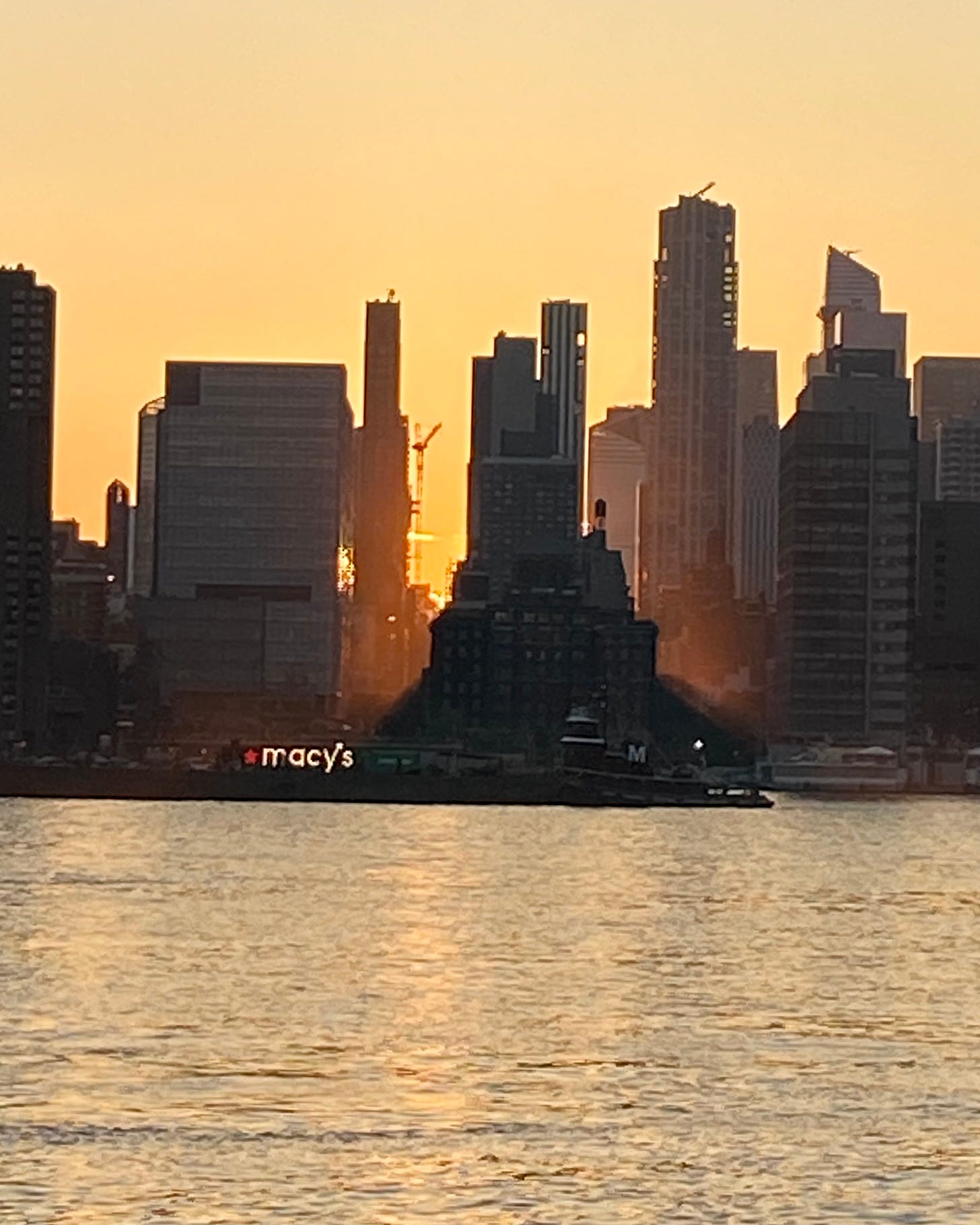 The sun setting as the Macy's barge on the East River begins to shine.