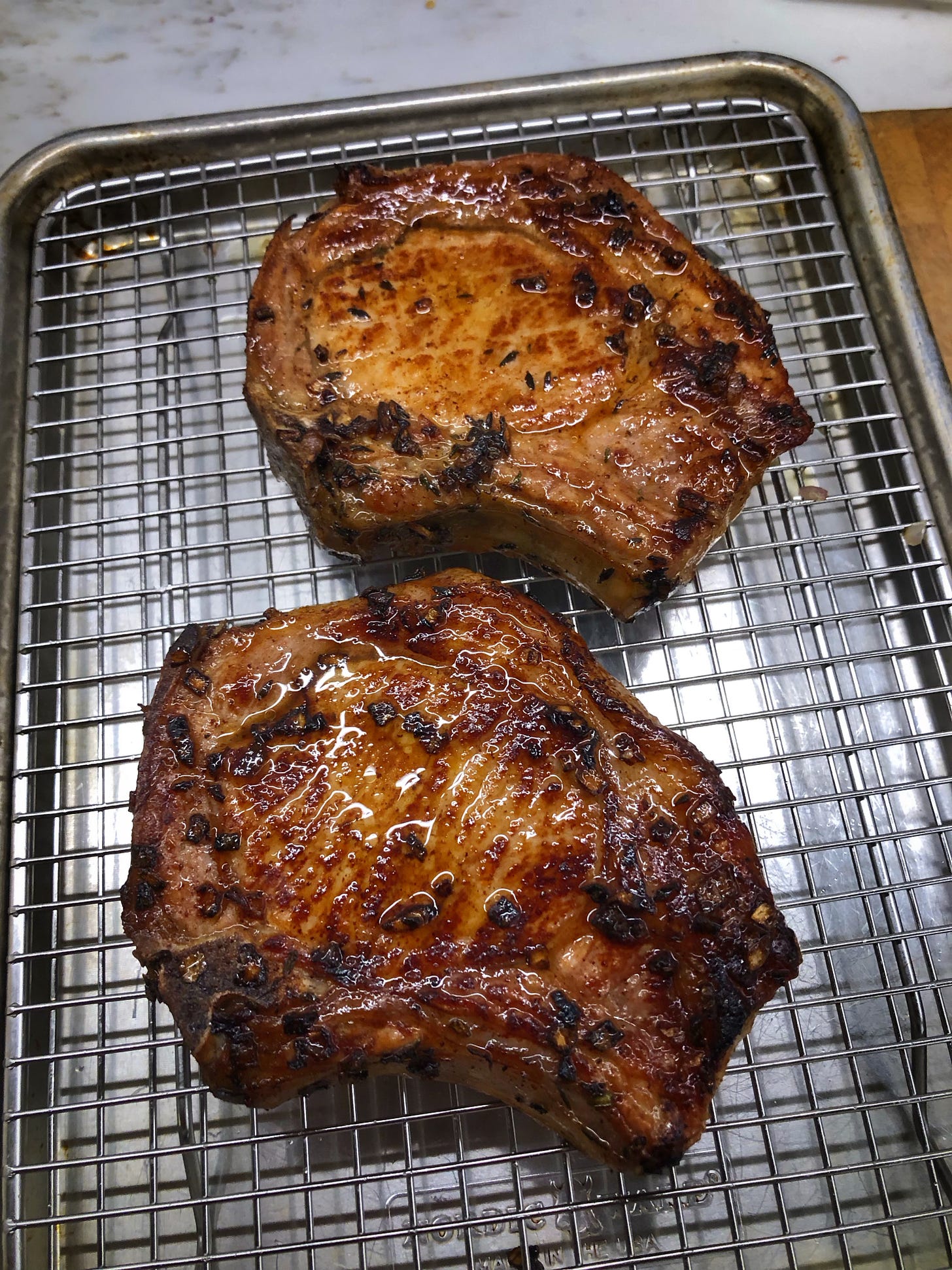 Two  cooked pork chops on a rack over a sheet pan.