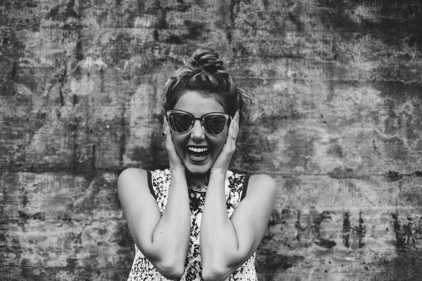 black and white picture of a woman smiling and covering her ears while wearing vintage sunglasses