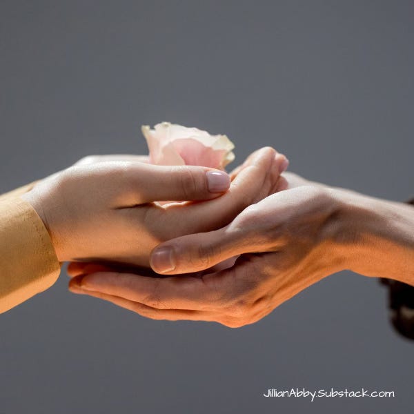 Two people's hands cupped together and holding a pink flower.