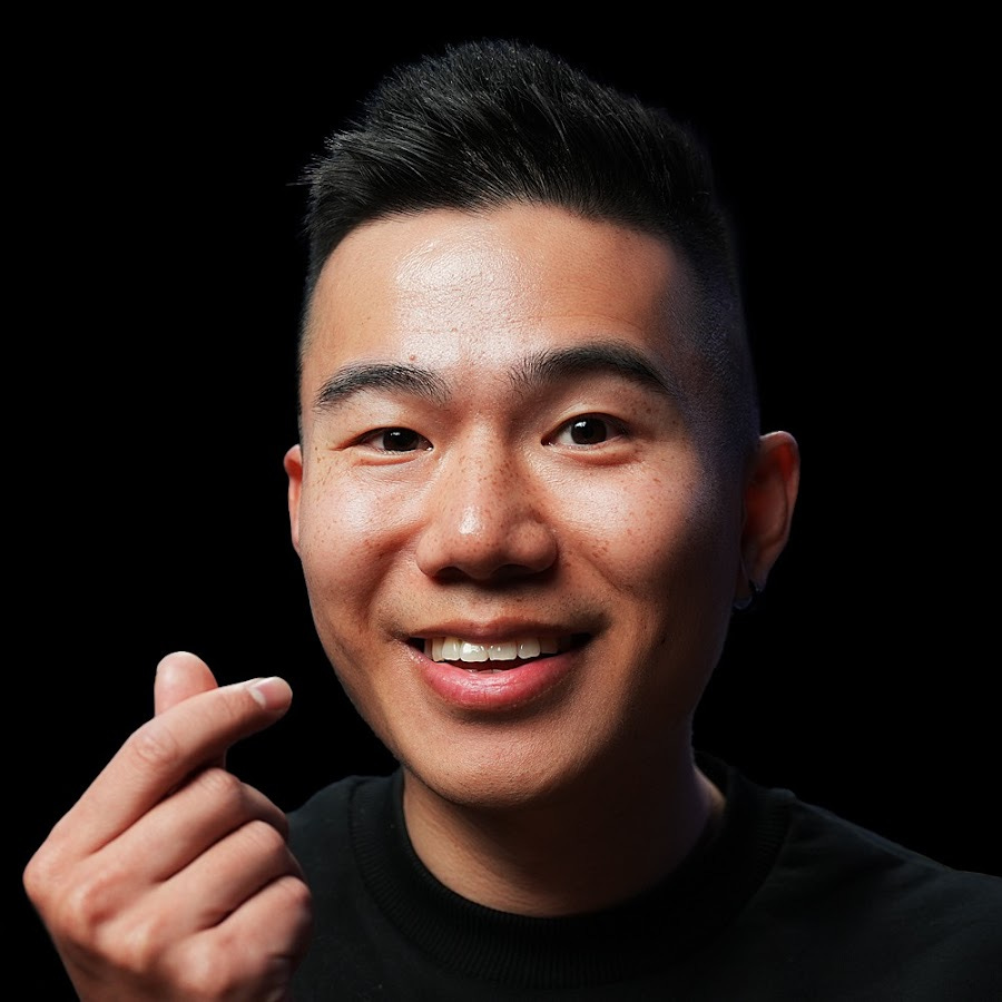 A portrait of an asian man holding up a heart sign with a black background