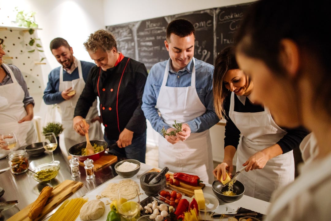 cooking class with a chef overseeing a group of people in white aprons