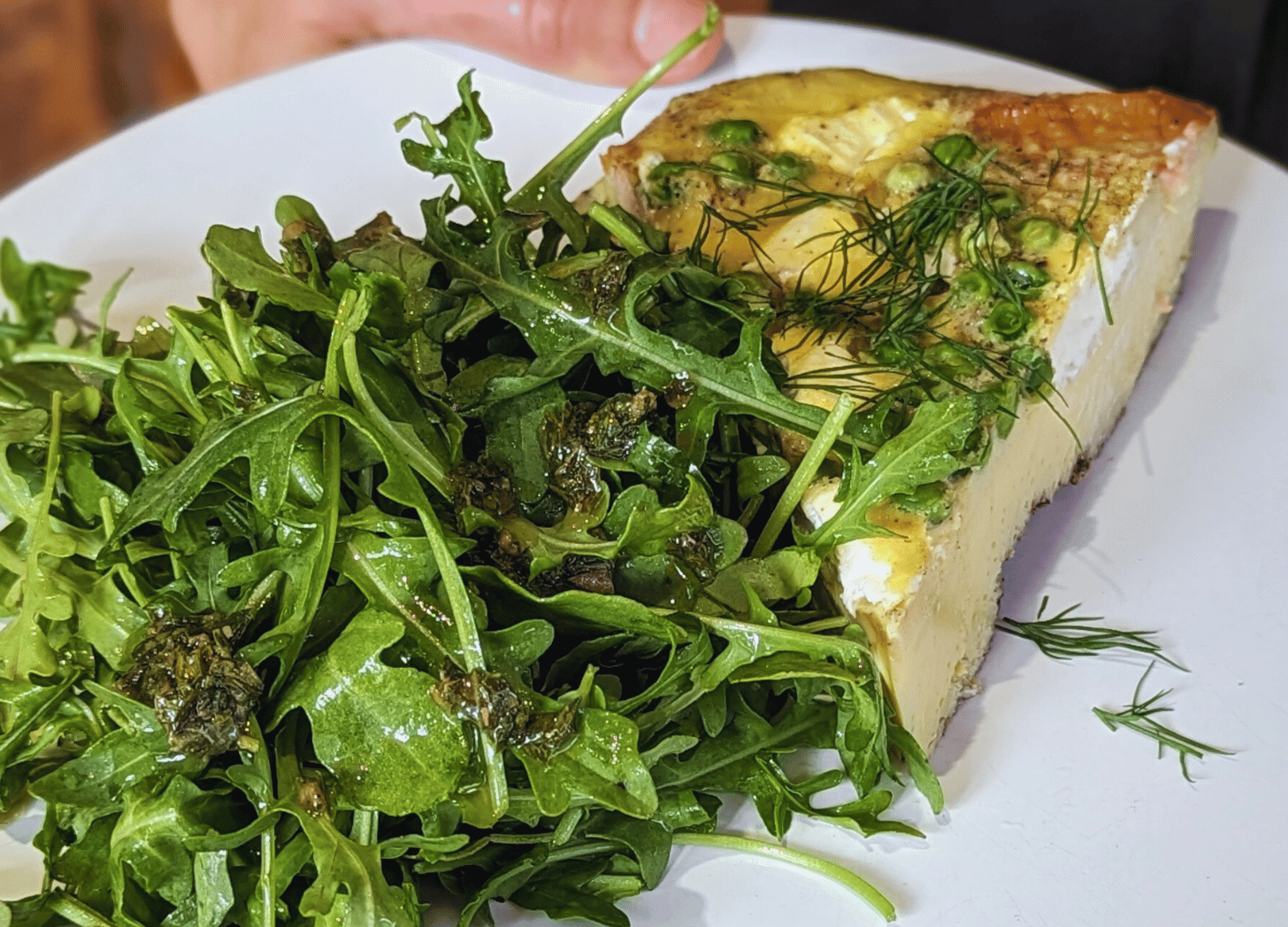 - a pile of fresh arugula with dill and an herb vinaigrette piled high beside a piece of frittata - you can see the ricotta cheese, a bit of smoked salmon and the spring peas on top. 