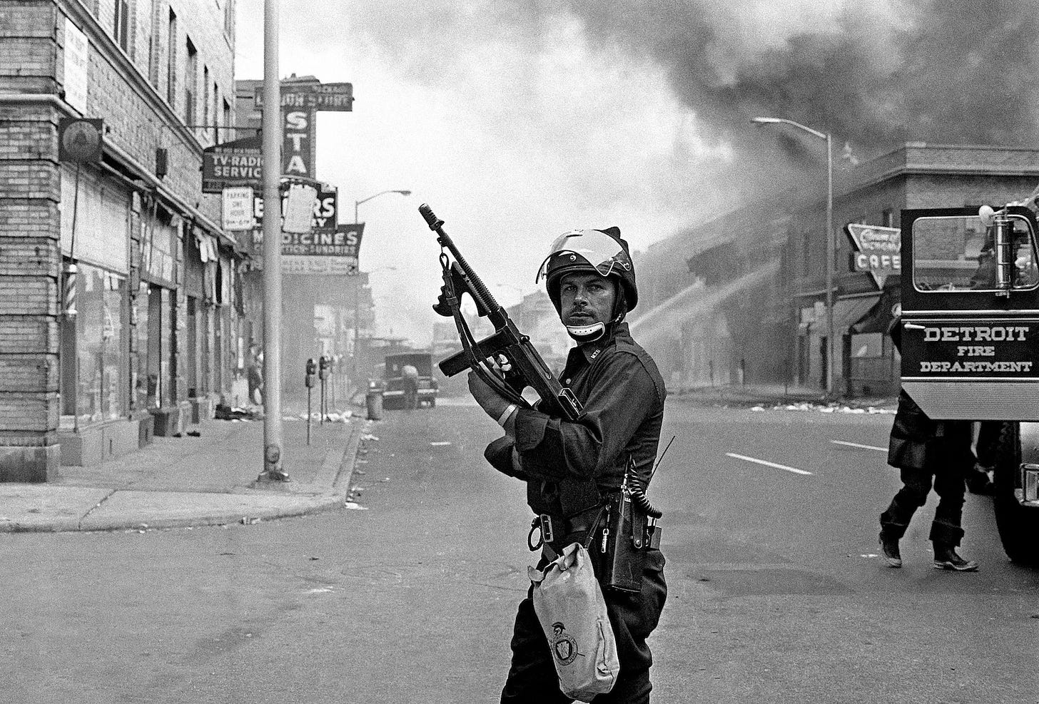 Helmeted cop with automatic weapon in the air stands in the middle of an intersection as smoke from arson fills the sky.