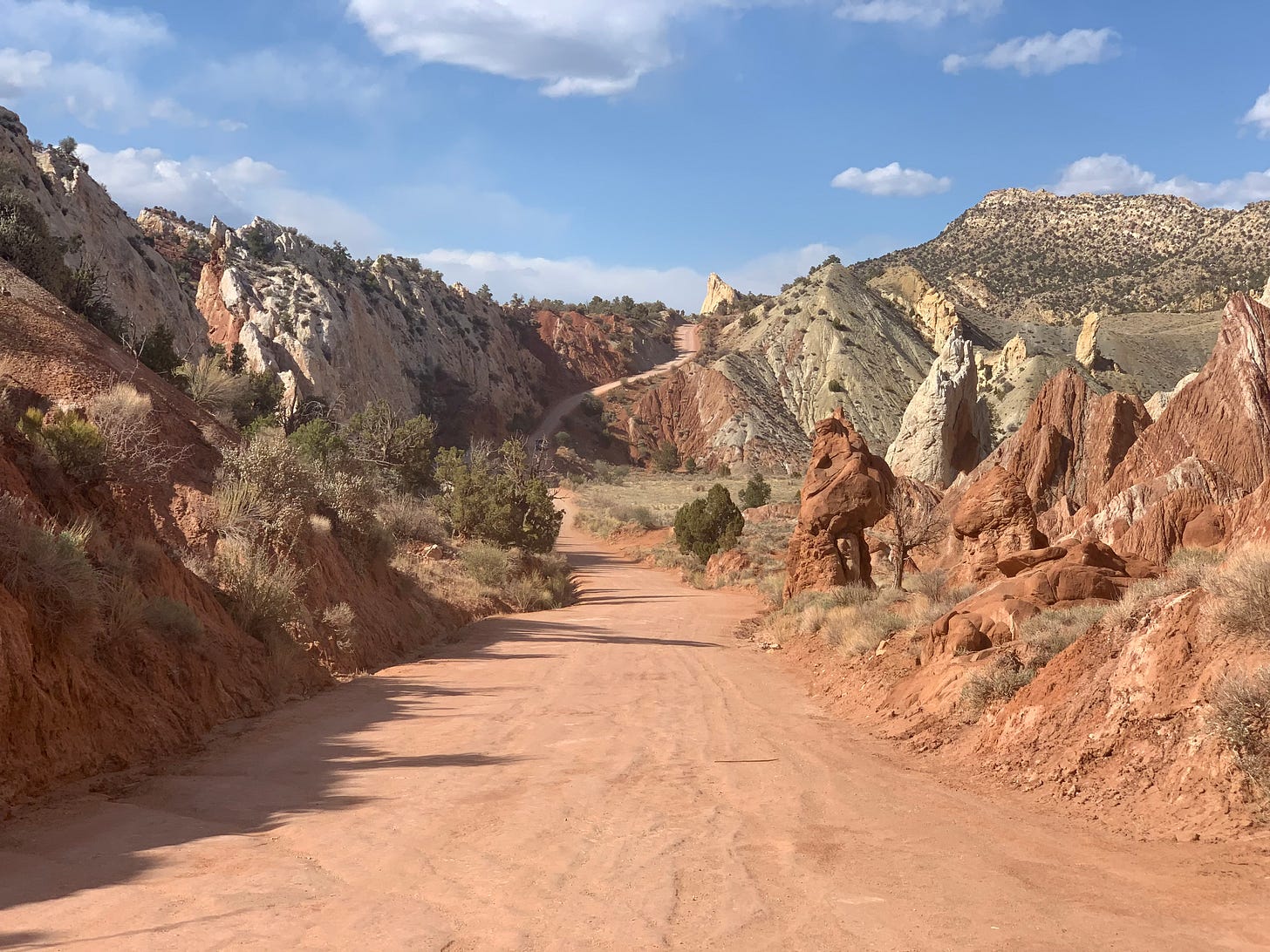 An empty dirt road winding through sandstone and shale rock formations 