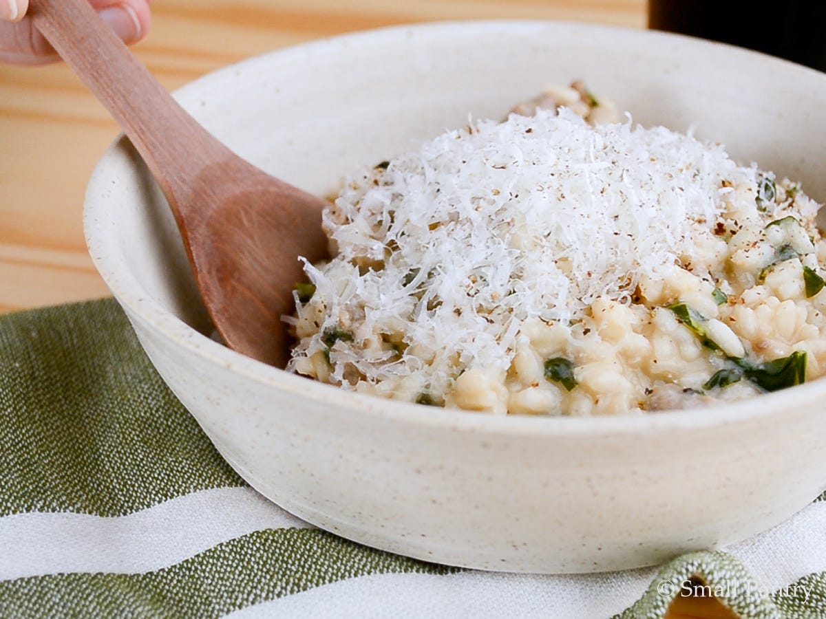 Bowl of sausage risotto with greens, topped with Parmesan