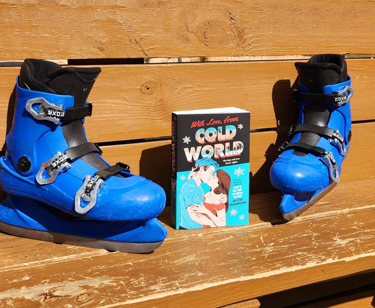 A copy of the teal cover copy of WITH LOVE, FROM COLD WORLD propped up in between two blue ice skates