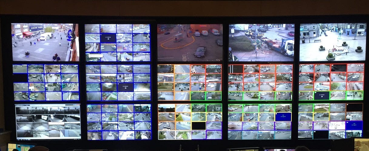 5x3 grid of mounted display monitors showing assorted CCTV footage, some in 4x4 grids of video channels