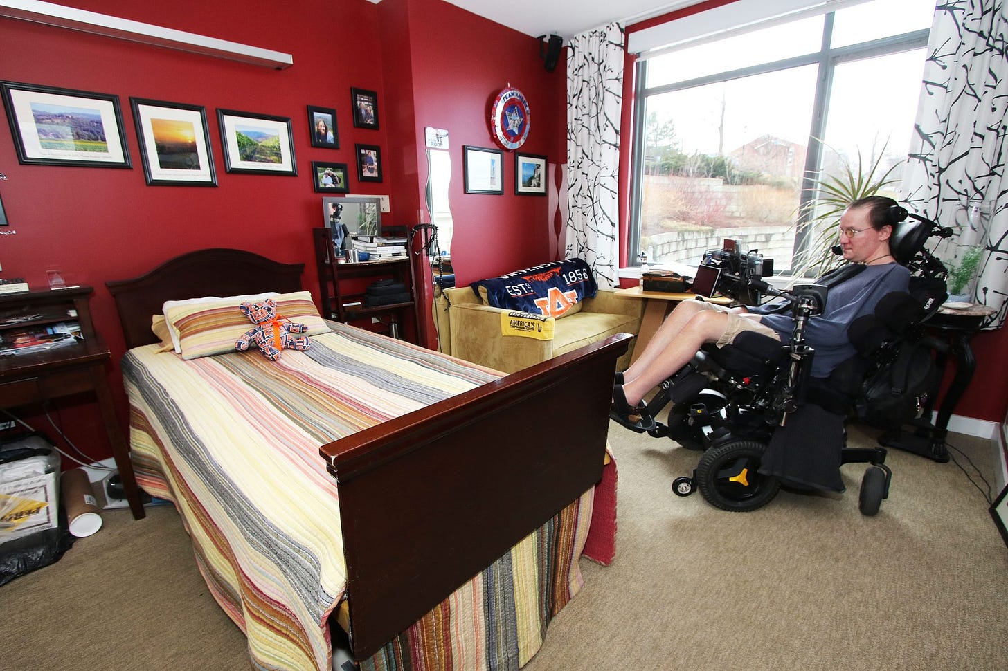 Steve Saling sits in a motorized wheelchair in his residence hall room, which has bright red walls, his chosen artwork and personal linens and curtains.