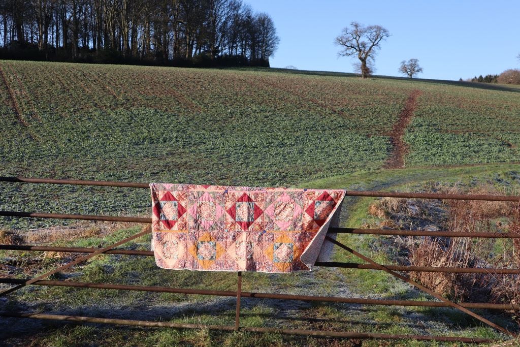 Patchwork blanket hanging over a farmer's gate. A ploughed field in the background. Fallow Fields - an article by Bex Massey of Bramble and Fox