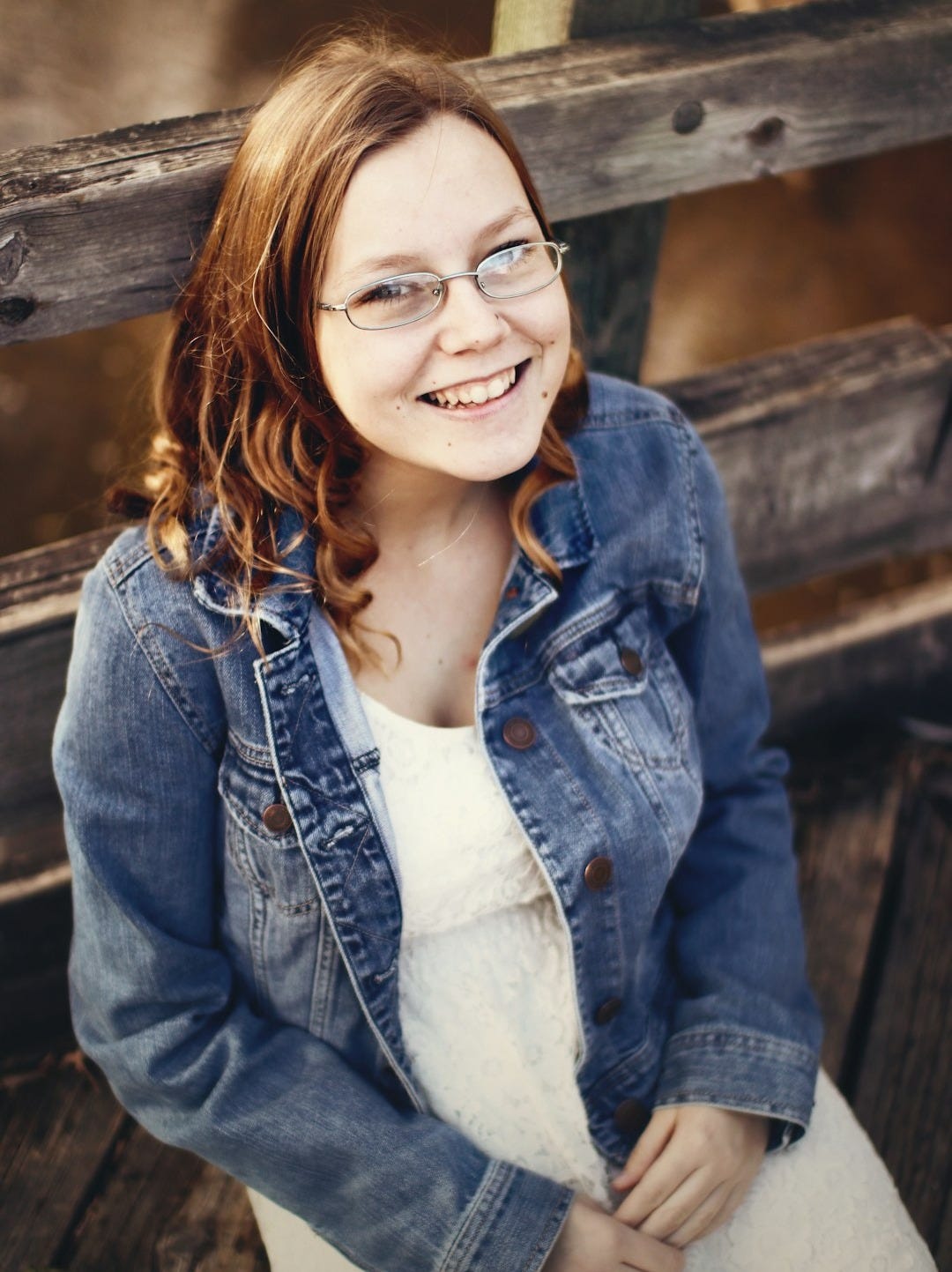 smiling woman wearing blue denim jacket and eyeglasses sitting on brown wooden bench