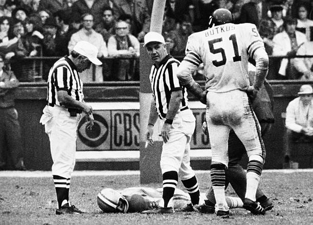 Detroit Lions' wide receiver Chuck Hughes lies on the field at Tiger Stadium, October 24, as the Chicago Bears' Dick Butkus and two officials await...