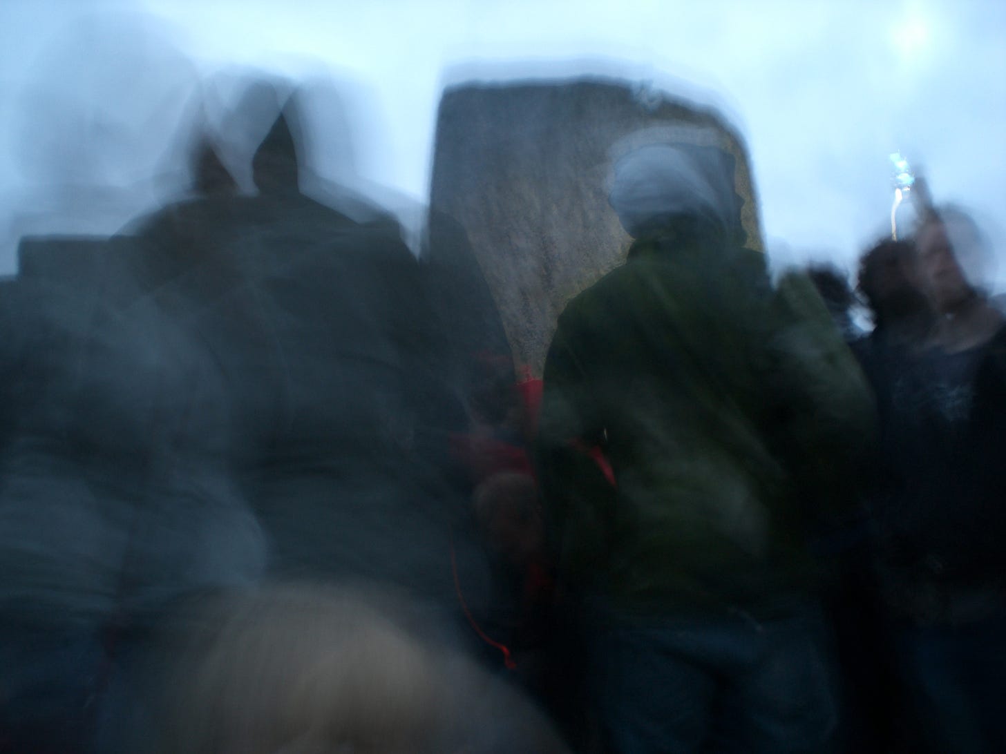 Blurry photo of a group of people at dawn a Stonehenge stone in the background.