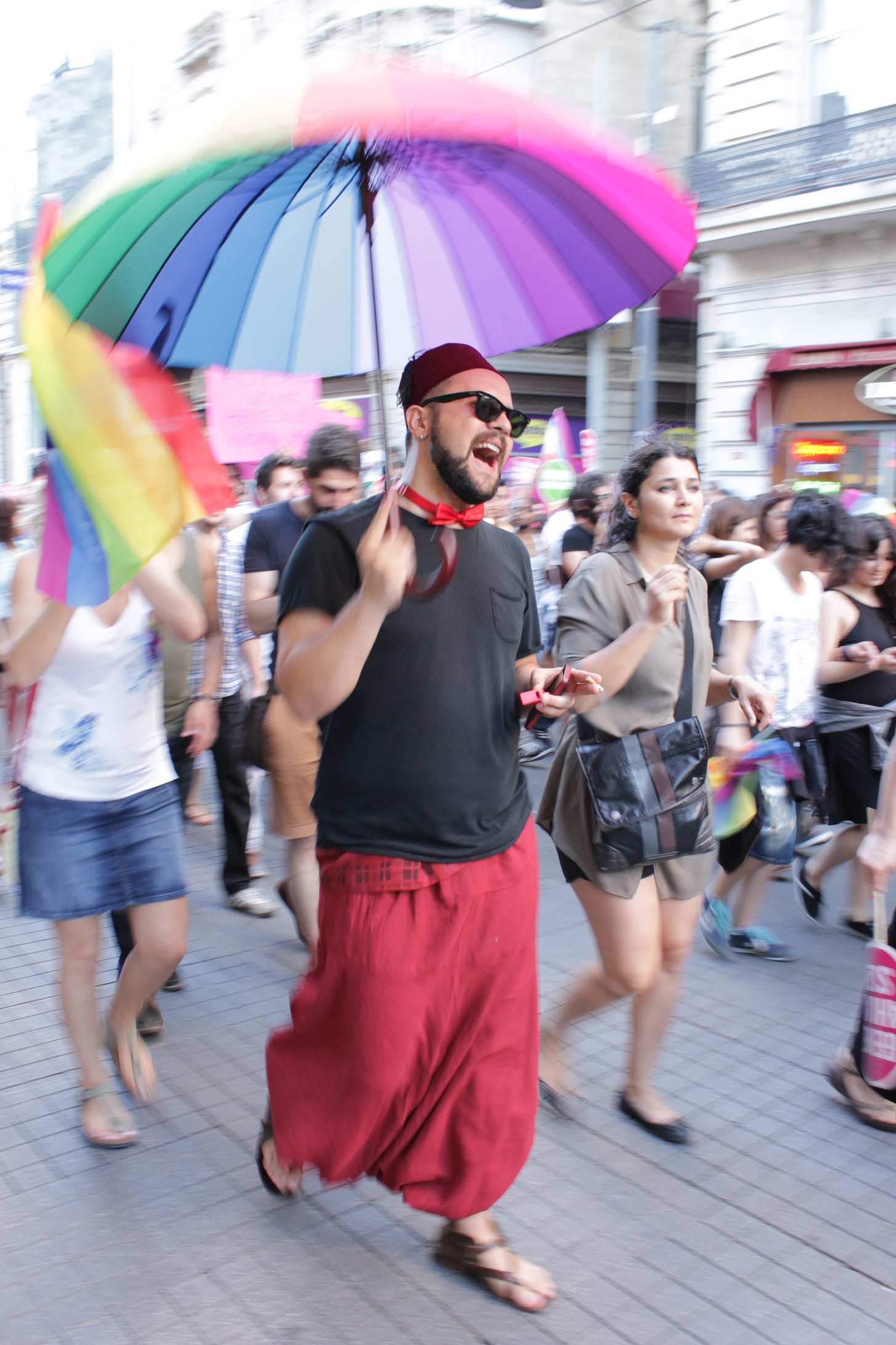 A man wearing a fez and holding a rainbow umbrella in Istanbul