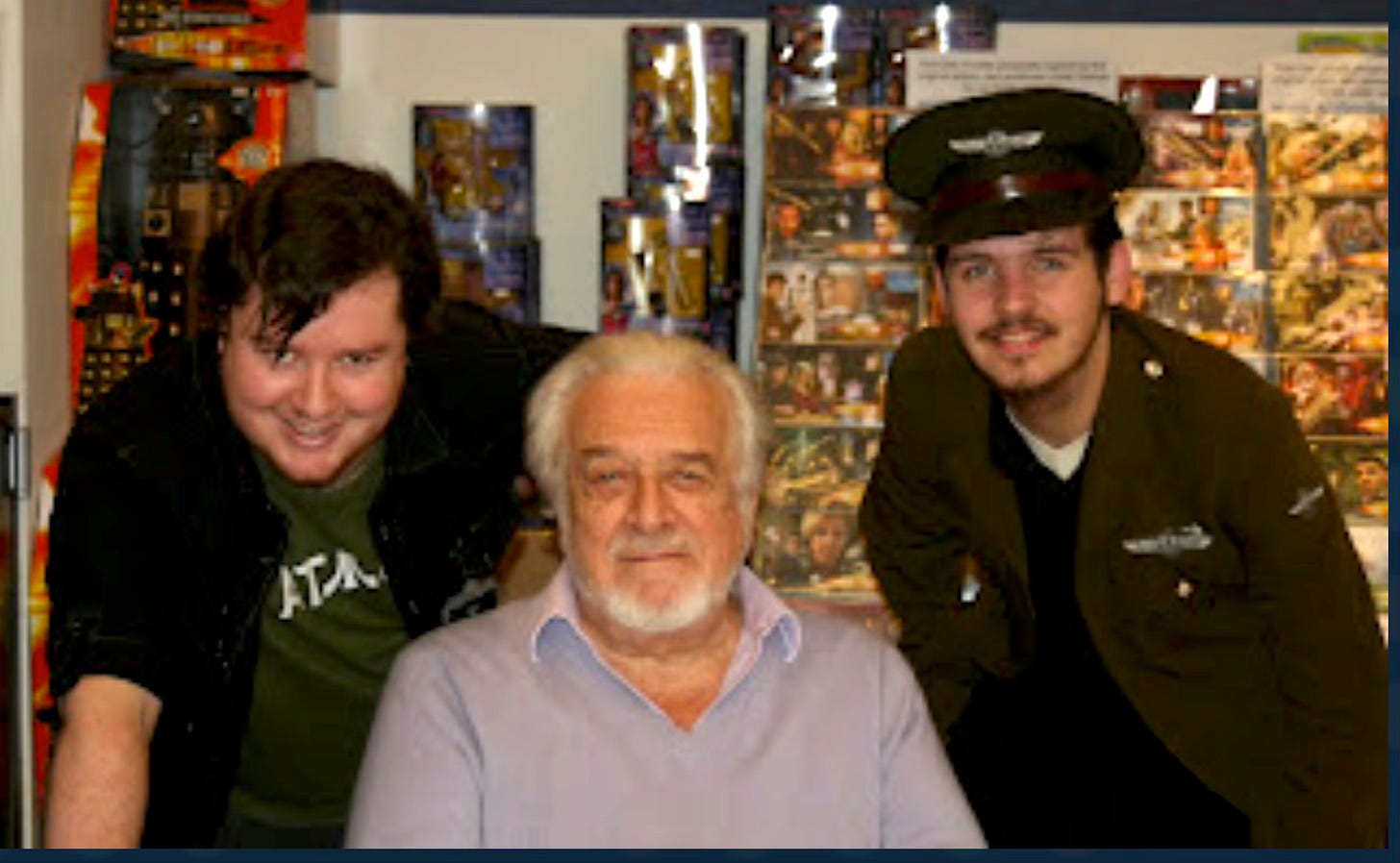 Alex, Nic Courtney, and Will in front of a display of Doctor Who merchandise