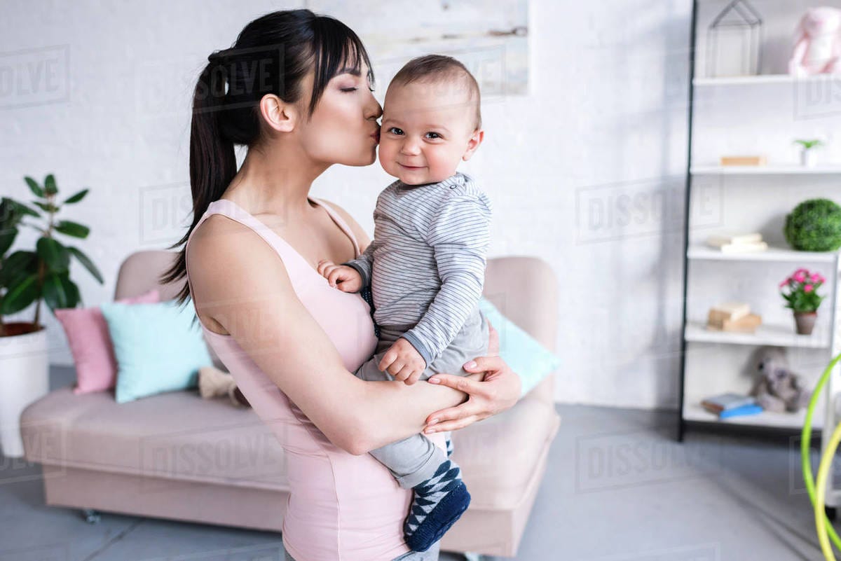 Beautiful young mother kissing her little child at home - Stock Photo -  Dissolve