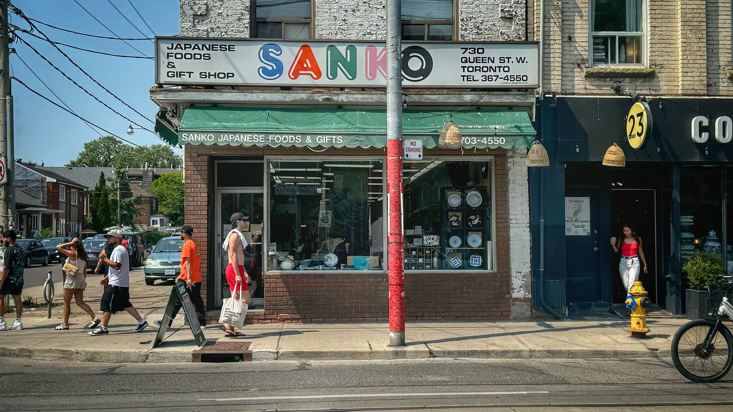 A street-level view of the Sanko storeforent. The sign reads "Japanese Foods & Gift Shop" and "730 Queen St W. Toronto. Tel 367-4550"