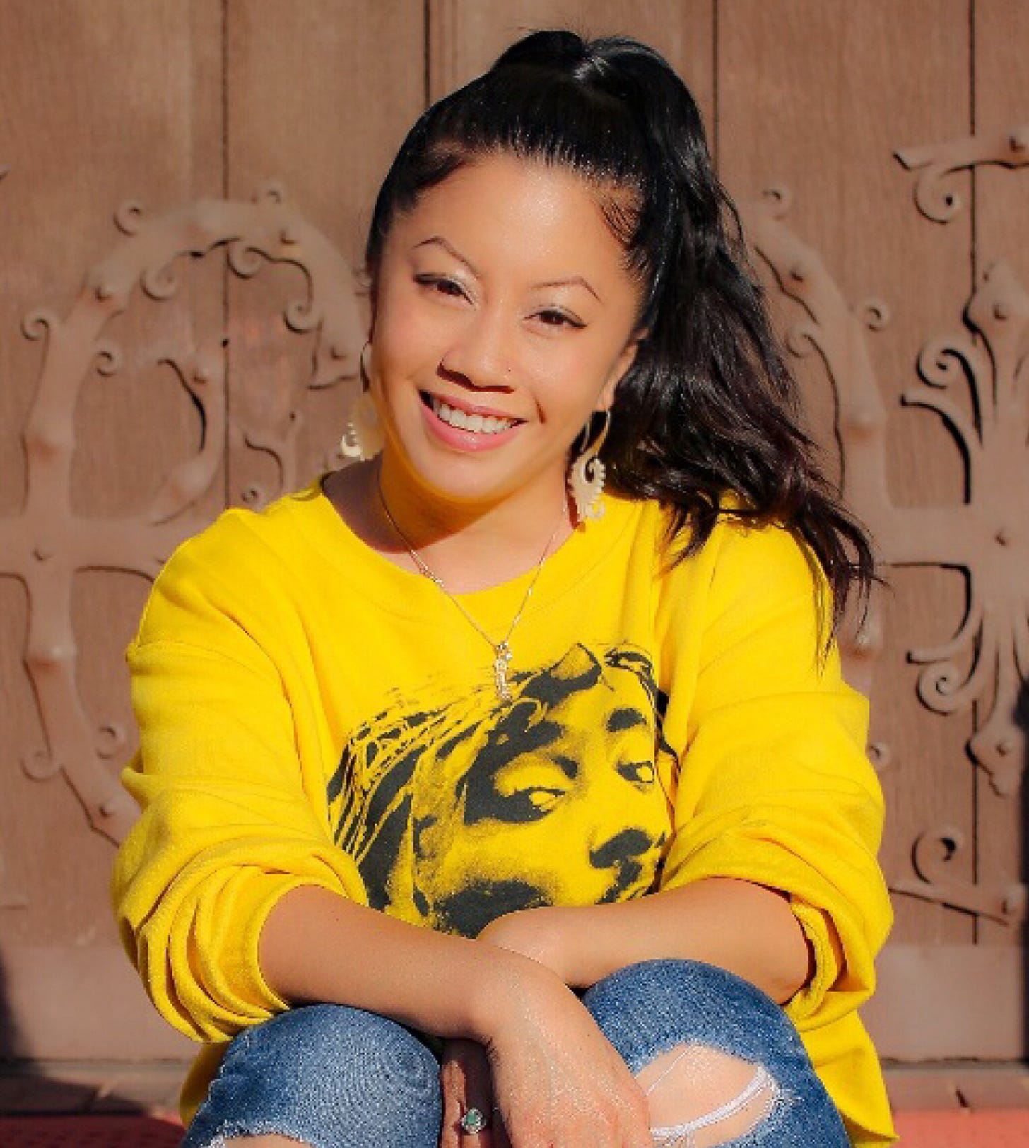 Nicole smiling, hair in a high ponytail, wearing yellow sweatshirt with Tupac Shakur image
