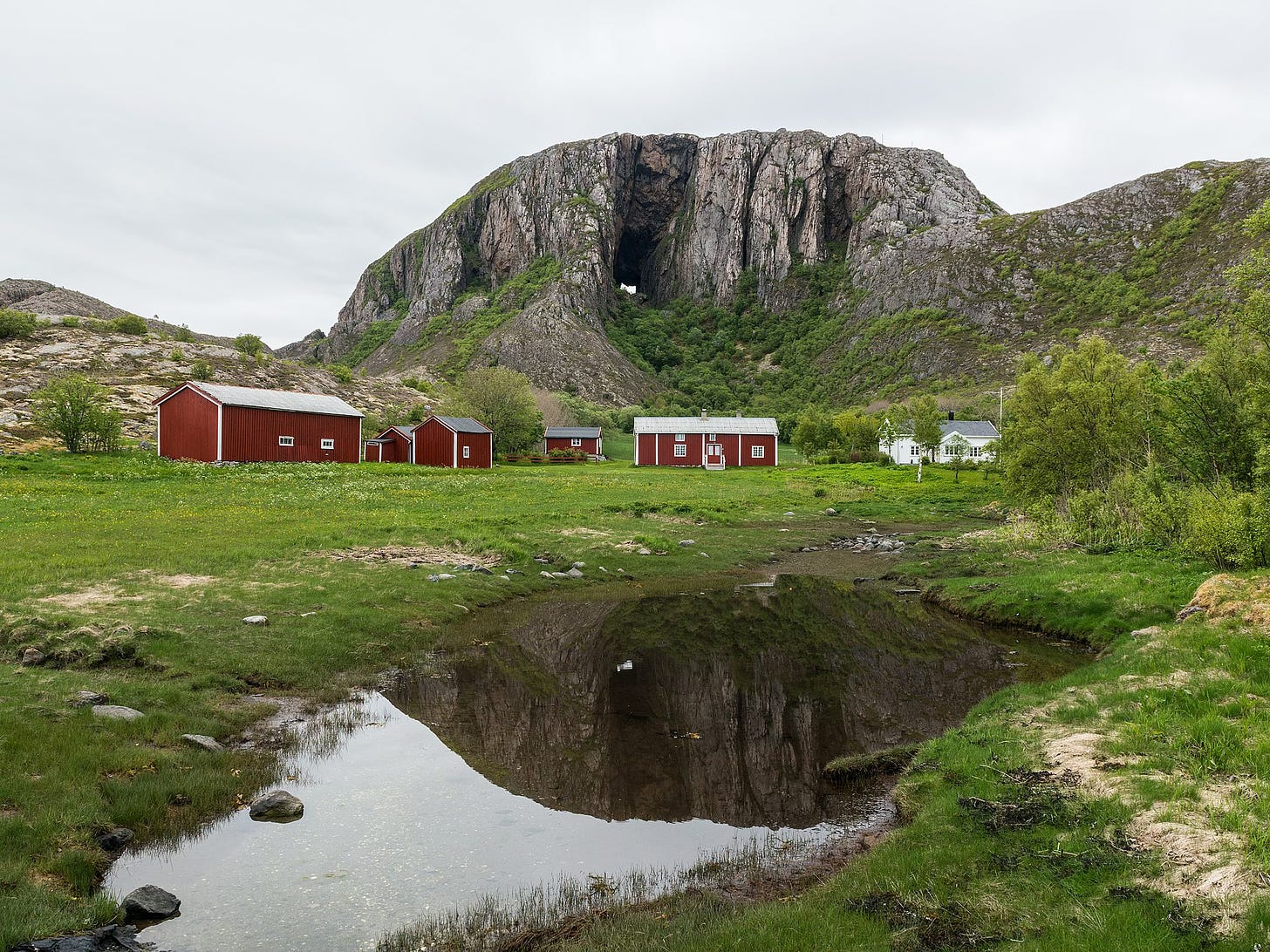 Photo of a giant granite rock with a hole in it above a green valley and red houses.