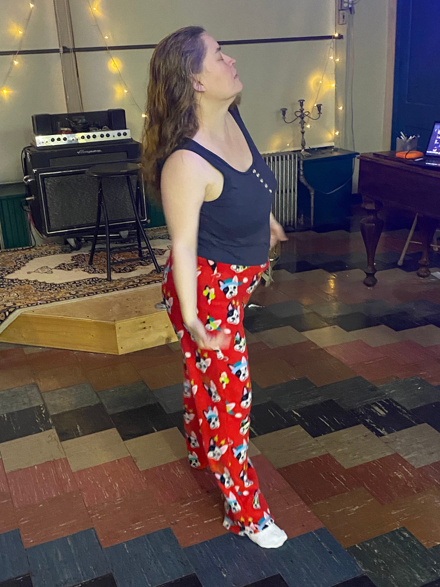 A femme presenting person dancing in a studio in red fuzzy pajama pants and a tank top